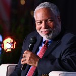 A man in a suit smiling holding a microphone.