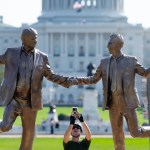 A man holding an iPhone holding a sculpture of two men holding hands and dancing.