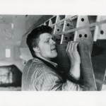 A man raises a piece of wood and sticks out his tongue.