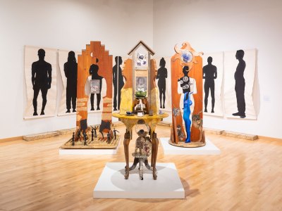 The table has multiple installed views of various objects found, two sculptures with figures and nine sculptures with wall-mounted paintings with black outlines. 