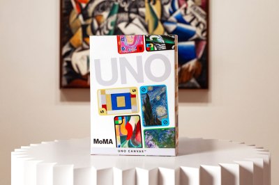 A box for the UNO deck sits on a pedestal in front of a painting with several cards printed on it.