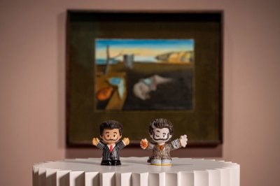 Two Salvador Dalí statues sit on pedestals in front of a Dalí painting.