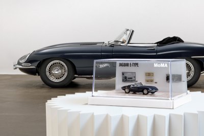 A replica of the naval sports car sits on a pedestal in front of the car that inspired it.