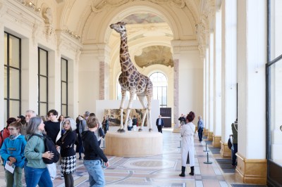 There is a giraffe sculpture on a pedestal among the crowd.