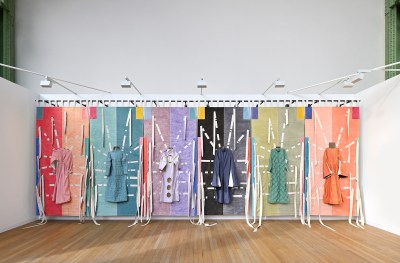 An installation composed of robe-like garments in varying colors hanging a multipart textile.