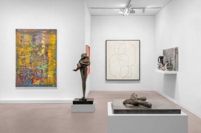 A fair booth with a sculpture of two hands, a sculpture of a person carrying a child, and an abstract painting.