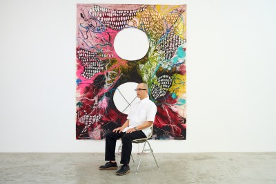 A man sits on a chair in front of an abstract painting.