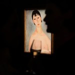 A painting of a woman with a man standing in the shadows holding a wine glass in front of the painting.