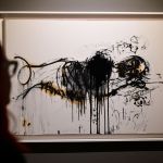 A woman looks at a painting of a man lying down.