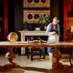 A woman stands behind a large marble dining table reading.