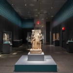 A dimly lit gallery with a statue of a pharaoh and god in the center.
