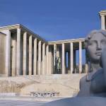 There is a columnar building surrounding the square with a sculpture of a woman in front.