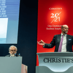Two men sell art behind a podium at an auction.