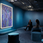 Two people in the blue room are looking at a painting by Matthew Wong.