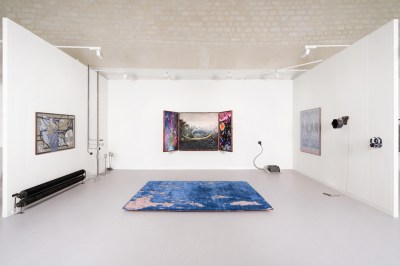 A fair both with an altarpiece-like artwork on one wall and a tattered rug in its center on the floor.