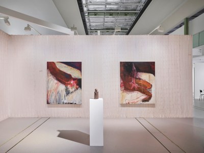 A fair booth with abstract paintings of women's bodies and a small wood sculpture on a plinth.