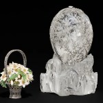 a crystal egg covered with a frost design, with a small basket of yellow and white flowers next to is that can hang inside the crystal egg