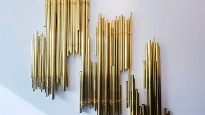 A wall-hung installation composed of brass tubes strewn with brass wire.