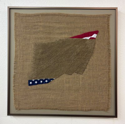 An artwork featuring a mostly covered US flag with dark burlap mounted onto lighter burlap.