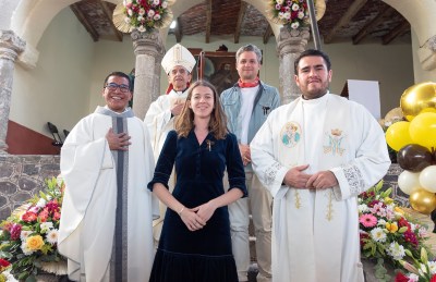 Three clergy and two lay people posed for a group photo with a painting in the background. 