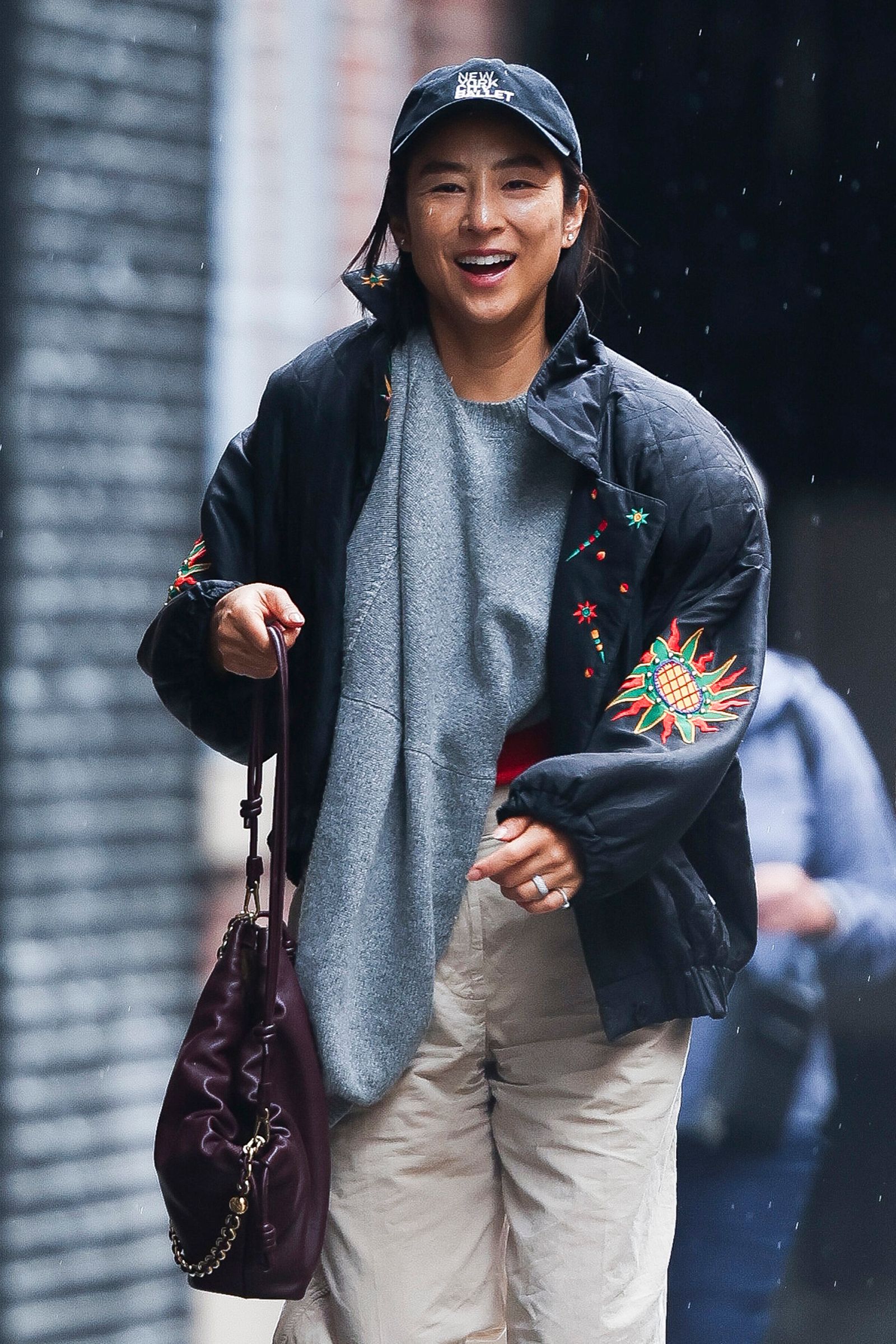 The image may contain Greta Lee face Happy Head Person Smile accessories bag handbag jewelry ring clothes and pants