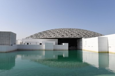 Exterior of a white building with gray lattice dome roof on a green-blue lake. 