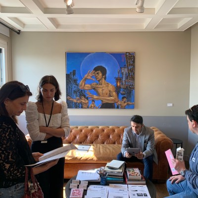 A photo shows several people in a hotel room with a painting on the wall showing Bruce Lee repeatedly shirtless in a fighting pose