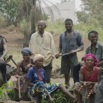 A group of African artists and plantation workers take photos outdoors with a museum building in the background