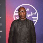 Portrait of Steve McQueen, a black man wearing a black suit standing on the red carpet.