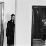 A man in a coat stands next to a painting.