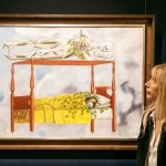 A woman stares at a painting of a woman lying on a bed under a canopy with a skeleton lying on top.