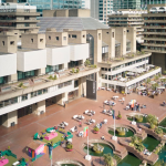 There is a concrete building with a fountain by the lake.