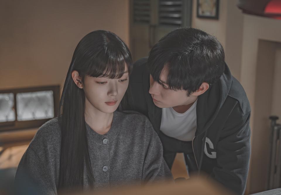 A man leans toward a woman sitting at a desk.