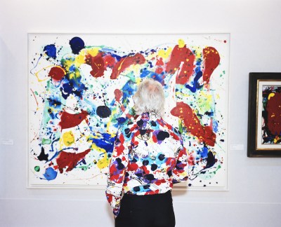 A woman wearing a shirt with black, red and purple spots, like an abstract painting she is looking at.