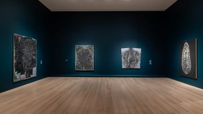 A gallery with blue walls hung with abstract paintings.