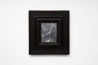 A small aluminum plate with a warped shape within a thick black frame.