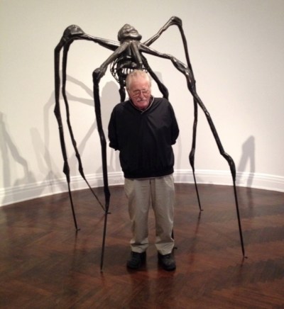 A man poses with a bronze spider sculpture. 