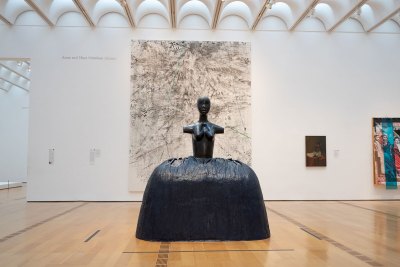 Installation view of a large sculpture of a black woman wearing a hoop skirt. She is topless and has no arms.