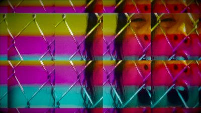 A still of a woman screaming behind a chainlink face that has a kaleidoscope effect.