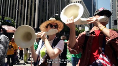 A video still of people blowing into horns with hands where the mouthpiece is.