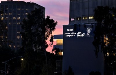 A projection on a building reading: 'TAKEN / Abelino, selling orange juice / Am I Next?'
