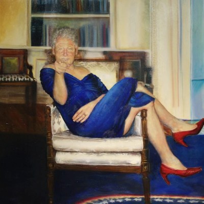 The painting shows a smiling man wearing a blue dress and red high heels sitting cross-legged on a chair, smiling and pointing a finger at the viewer.