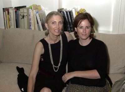 Two women seated together on a couch with books behind it.