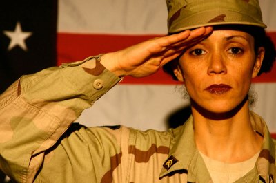 A woman in an army uniform stands in front of the US flag and does a salute. 