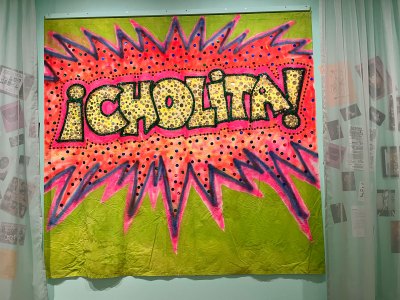 A banner reading '¡Cholita!' hangs on a museum wall. 
