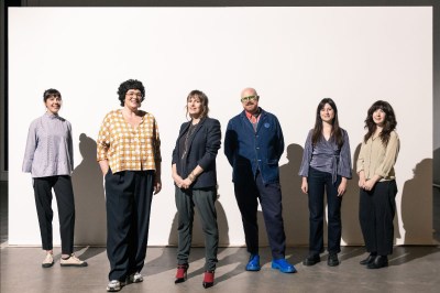 Six people stand in front of a white false wall.