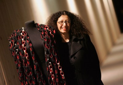 Portrait of Amina Aguenzay standing beside a mannequin with a weaving slung around its shoulders.