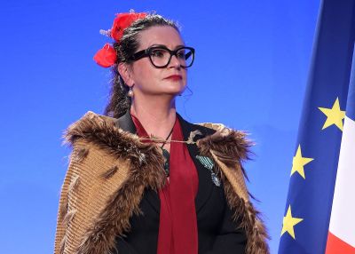 An Indigenous woman with flowers i her hair and a wrap across her shoulders.