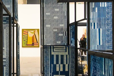 An installation composed of bluish weavings on an armature. A person can be seen taking pictures of it.