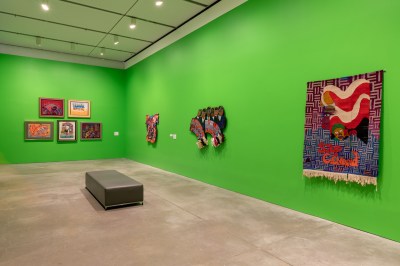 Abstract textiles hang on the green walls.